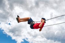 Side view of boy on a swing with only cloudy sky in the background. — Stock Photo