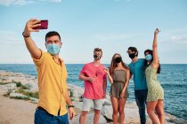 Um grupo de jovens usando máscara facial para coronavírus na praia — Fotografia de Stock