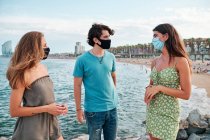 Dos mujeres jóvenes y un hombre con mascarilla en la playa de Barcelona - foto de stock