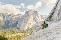 Молодой человек, сидящий на горе Эль-Капитан, смотрит на парк Йосемити — стоковое фото