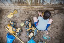 Jeune garçon jouant dans un bac à sable boueux dans la cour arrière remplie de jouets. — Photo de stock