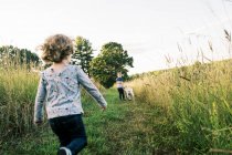 Zwei Kinder mit ihrem Welpen bei einem Sommerabendspaziergang auf einem Feld — Stockfoto