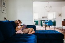 Cute little girl with tablet sitting on sofa - foto de stock
