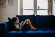 Милий маленький хлопчик використовує планшет на дивані — стокове фото