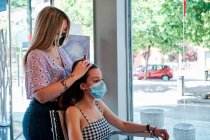Un coiffeur portant un masque facial faisant des boucles au salon beatuy - concept de crise coronavirus — Photo de stock