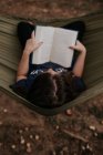 Sobrecarga vertical de la muchacha adolescente que se sienta en lectura de la hamaca - foto de stock