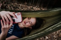 Девочка-подросток, лежащая в гамаке и играющая по мобильному телефону — стоковое фото