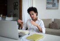 Señora negra gesticulando y utilizando el ordenador portátil para hablar con sus colegas en línea desde casa - foto de stock