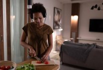 Felice donna afroamericana ascoltando musica e tagliando pomodori per cena a casa — Foto stock