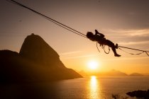 Beautiful sunrise view of man walking on highline with Sugar Loaf Mountain and ocean on the back, Rio de Janeiro, Brazil — Stock Photo