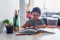 Латиноамериканська дівчинка малює на столі з олівцями та кольорами.. — стокове фото