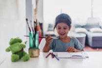 Spanisches Mädchen malt mit Bleistiften und Farben auf dem Schreibtisch. — Stockfoto