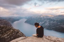 Uomo che guarda giù curioso seduto nella roccia sul bordo della scogliera a Preikestolen, Norvegia — Foto stock