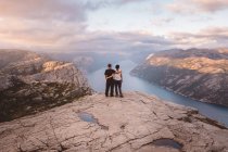 Пара стоїть на скелі в Преікестолен, Норвегія під час заходу сонця. — стокове фото