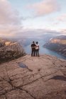 Coppia in piedi e di fronte a vicenda a scogliera a Preikestolen, Norvegia durante il tramonto — Foto stock