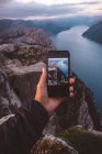 Handhaltendes Smartphone mit Bild der Szene im Hintergrund in den norwegischen Fjorden. — Stockfoto