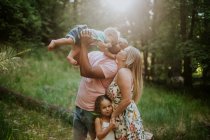 Familia de cuatro acurrucarse y besarse en el bosque - foto de stock