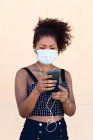 Черная женщина в маске управляет своим мобильным телефоном — стоковое фото