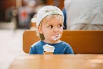 Jovem loira menino com rosto sujo comer sorvete com um boné em — Fotografia de Stock