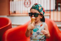 Jovem criança comendo sorvete cone com tampa para trás e óculos de sol — Fotografia de Stock