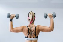 Rückenansicht der blonden Frau beim Training mit Kurzhanteln im Fitnessstudio — Stockfoto