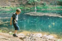 Un garçon de cinq ans jouant près d'un étang turquoise dans les bois — Photo de stock