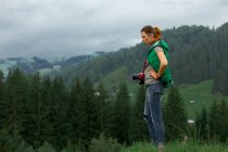 Chica fotógrafa en las montañas dispara el paisaje en el fondo de un día nublado - foto de stock