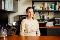 Une professeure souriante s'assoit à son bureau dans un bureau — Photo de stock