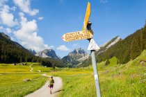 Uma mulher caminha por uma estrada de terra passando por um sinal de trilha em Smtisertal, um vale em Alpstein, Suíça. — Fotografia de Stock