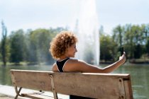 Femme sur un banc près du lac prendre un selfie — Photo de stock