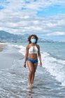 Femme afro-américaine marche sur la plage avec un masque — Photo de stock