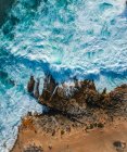 Vue aérienne du dessus des vagues de mer frappant des rochers sur la plage — Photo de stock