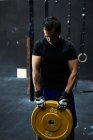 Young man lifting heavy disc at indoors garage-gym — Stock Photo