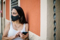 Pensive woman wearing face mask using a mobile phone in the street — Stock Photo