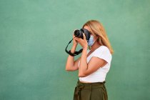 Giovane donna con una maschera e una macchina fotografica su sfondo verde — Foto stock