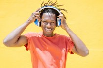 Happy ethnic man putting on headset and listening to music against yellow wall — Stock Photo