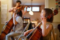 A happy child plays cello with family in background playing music — Stock Photo