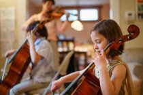 A small child plays cello concert with her family in the living room — Stock Photo