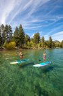 Un hombre y una mujer de pie paddle boarding en Lake Tahoe, CA - foto de stock