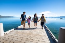 Eine Familie lächelt und hält Händchen, als sie an einem sonnigen Tag in South Lake Tahoe, Kalifornien, einen Steg hinunterläuft. — Stockfoto