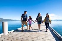 Eine Familie lächelt und hält Händchen, als sie an einem sonnigen Tag in South Lake Tahoe, Kalifornien, einen Steg hinunterläuft. — Stockfoto