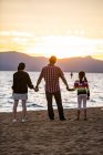 Ein Vater hält Händchen mit seinen Töchtern, während sie den Sonnenuntergang am Nevada Beach in Lake Tahoe, Nevada beobachten. — Stockfoto