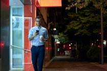 Молодой бизнесмен ходит со своим смартфоном и кофейной чашкой — стоковое фото