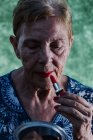 Old lady painting her lips in red looking at herself in the mirror — Stock Photo