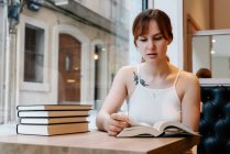 Молода жінка сидить у кафетерії читаючи книги — стокове фото
