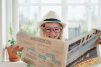 Молодая девушка смеется, читая газету в шляпе и очках — стоковое фото