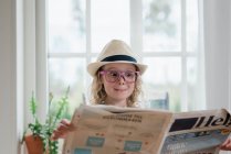 Jovem menina puxando caras engraçadas enquanto lia um jornal — Fotografia de Stock