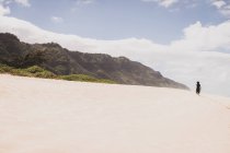 Woman walks up sandy hill towards the mountains — Stock Photo