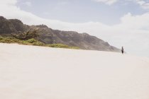 Mujer de pie en una colina de arena en frente de una montaña en la distancia - foto de stock