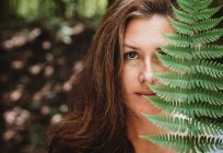 Portrait of a brunette woman covering half her face with a fern leaf. — Stock Photo
